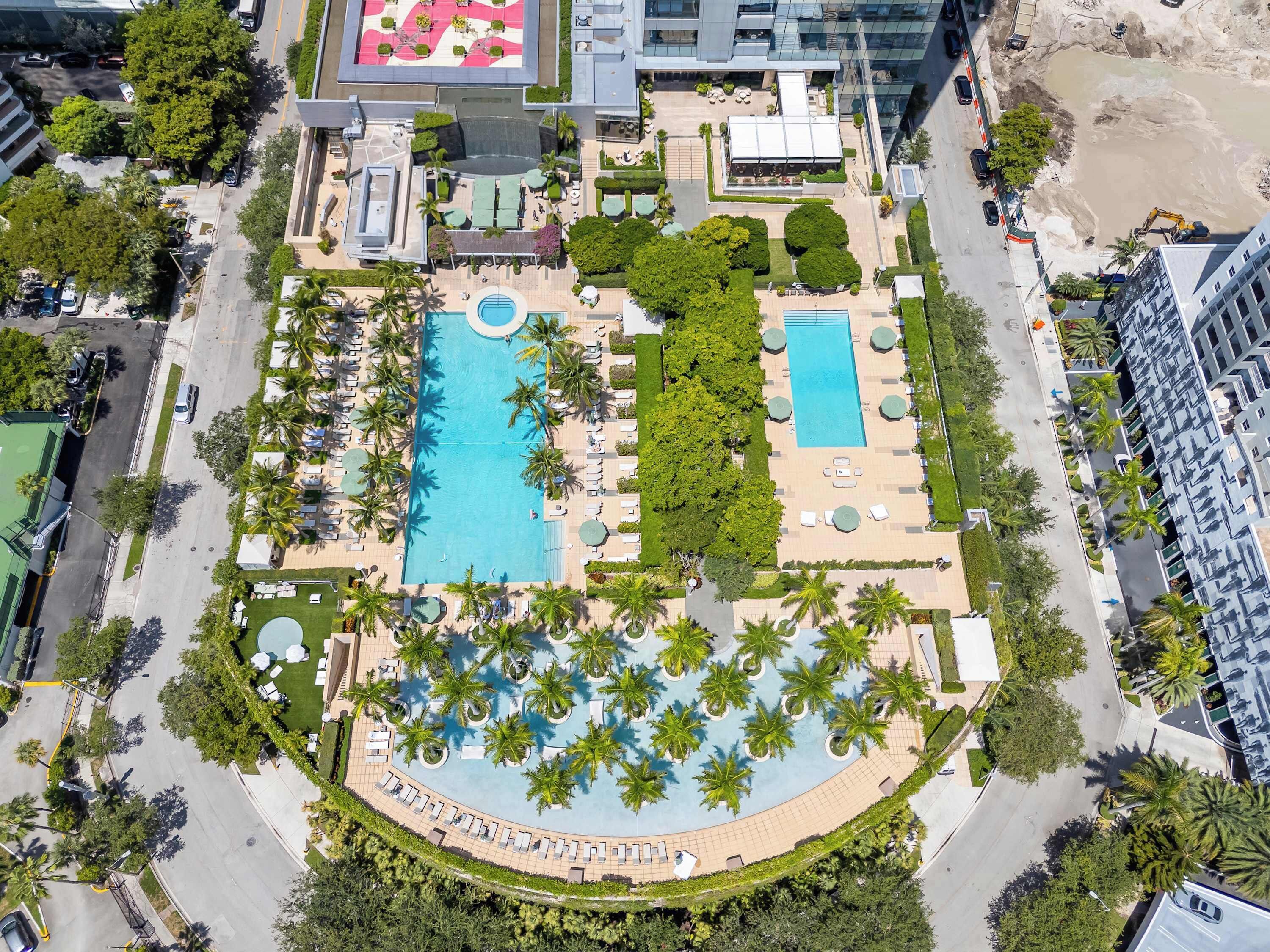 Vista aerea di un resort con due piscine, palme e aree verdi curate.