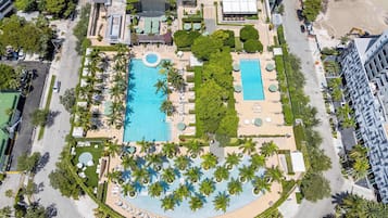An aerial view of a resort with two swimming pools, palm trees, and a landscaped area.