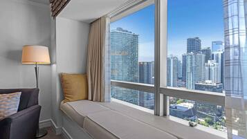 A room with a large window, a sofa, a lamp, and a view of a cityscape.