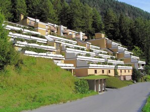 Eine Wohngegend an einem Hang mit modernen Häusern, einer Straße und dichtem Wald im Hintergrund.