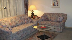 Ett vardagsrum med två soffor med blommönster, ett litet soffbord, en lampa och en inramad abstrakt målning på väggen.