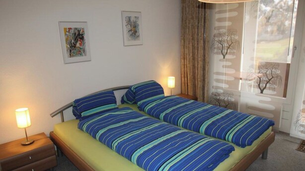 En dubbelsäng med randigt sänglinne, sänglampor och två inramade konstverk på väggen.