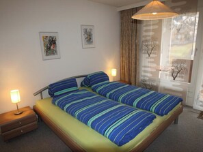 A double bed with striped bedding, bedside lamps, and two framed artworks on the wall. - Lärchenwald 1804 # 2-bed apartment, Dusche, WC 2-Bettwohnung, Dusche, WC by Interhome (Leukerbad)