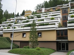 A modern hotel with a flat roof, multiple balconies with greenery, and a central entrance. - Lärchenwald 1804 # 2-bed apartment, Dusche, WC 2-Bettwohnung, Dusche, WC by Interhome (Leukerbad)