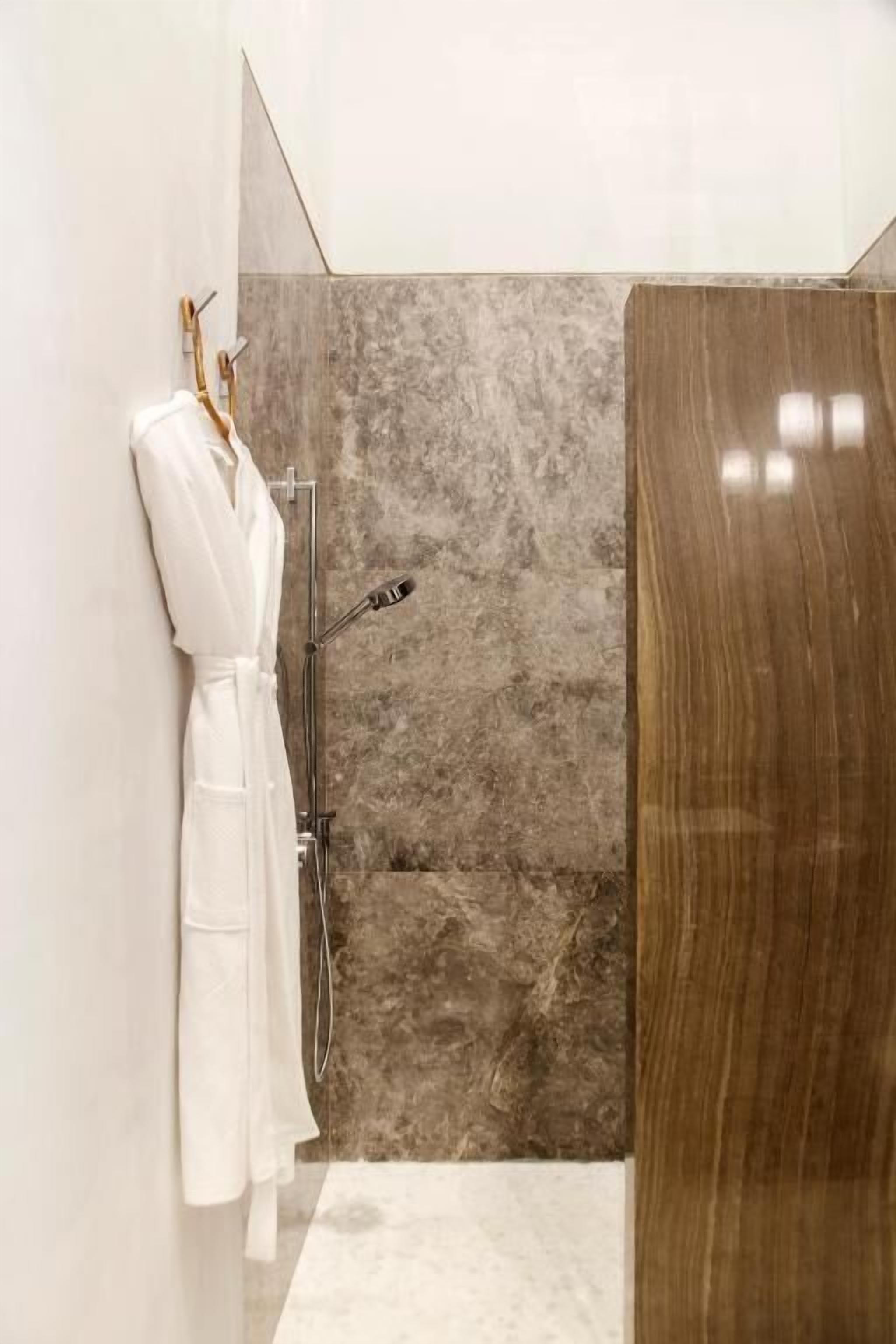 A modern bathroom with a shower, a wooden door, and a white robe hanging on a rack.