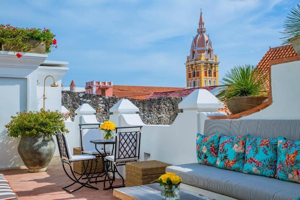 Terraço no telhado com área de refeições, um sofá com almofadas florais e vista para um edifício histórico.