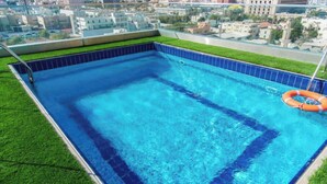 A rooftop swimming pool with clear blue water, surrounded by a tiled edge and a grassy border. - Emerald Twin Delight Sunday Emerald (Jeddah)
