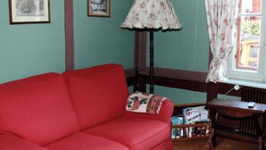 Um quarto com sofá vermelho, luminária, janela com cortinas e quadros nas paredes.