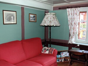 A room with a red sofa, a lamp, a window with curtains, and framed pictures on the wall. - Heimatkunst 1 (Lucia) # 5-bed apartment, Dusche, WC 5-Bettwohnung, Dusche, WC by Interhome (Leukerbad)