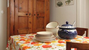 Uma sala de jantar com um armário de madeira, toalha de mesa floral, uma pilha de pratos e um bule azul e branco.