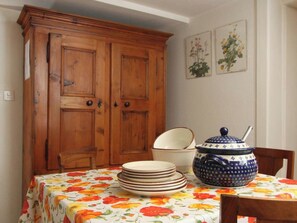 A dining area with a wooden cabinet, a floral tablecloth, a stack of plates, and a blue and white teapot. - Heimatkunst 1 (Lucia) # 5-bed apartment, Dusche, WC 5-Bettwohnung, Dusche, WC by Interhome (Leukerbad)