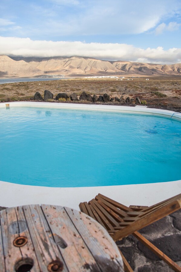 A pool with a wooden deck and lounge chairs, surrounded by a mountainous landscape.