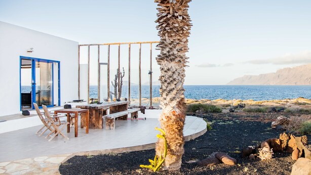 Una propiedad costera con zona de comedor, una palmera y vista al mar.