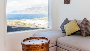 Una habitación con un ventanal grande, vigas de madera en el techo, un sofá color beige con cojines estampados y un barril de madera.