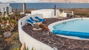 Zona de piscina con sillones de descanso, una mesita y vistas al mar y a las montañas.