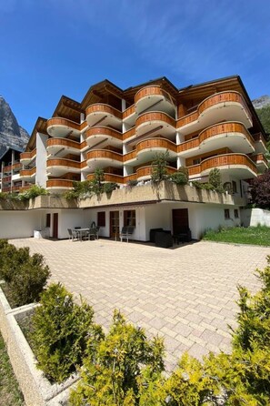 A multi-story hotel with balconies, a paved courtyard, and a mountainous backdrop. - Christina 20 # 4-bed apartment, Bad, WC 4-Bettwohnung, Bad, WC by Interhome (Leukerbad)