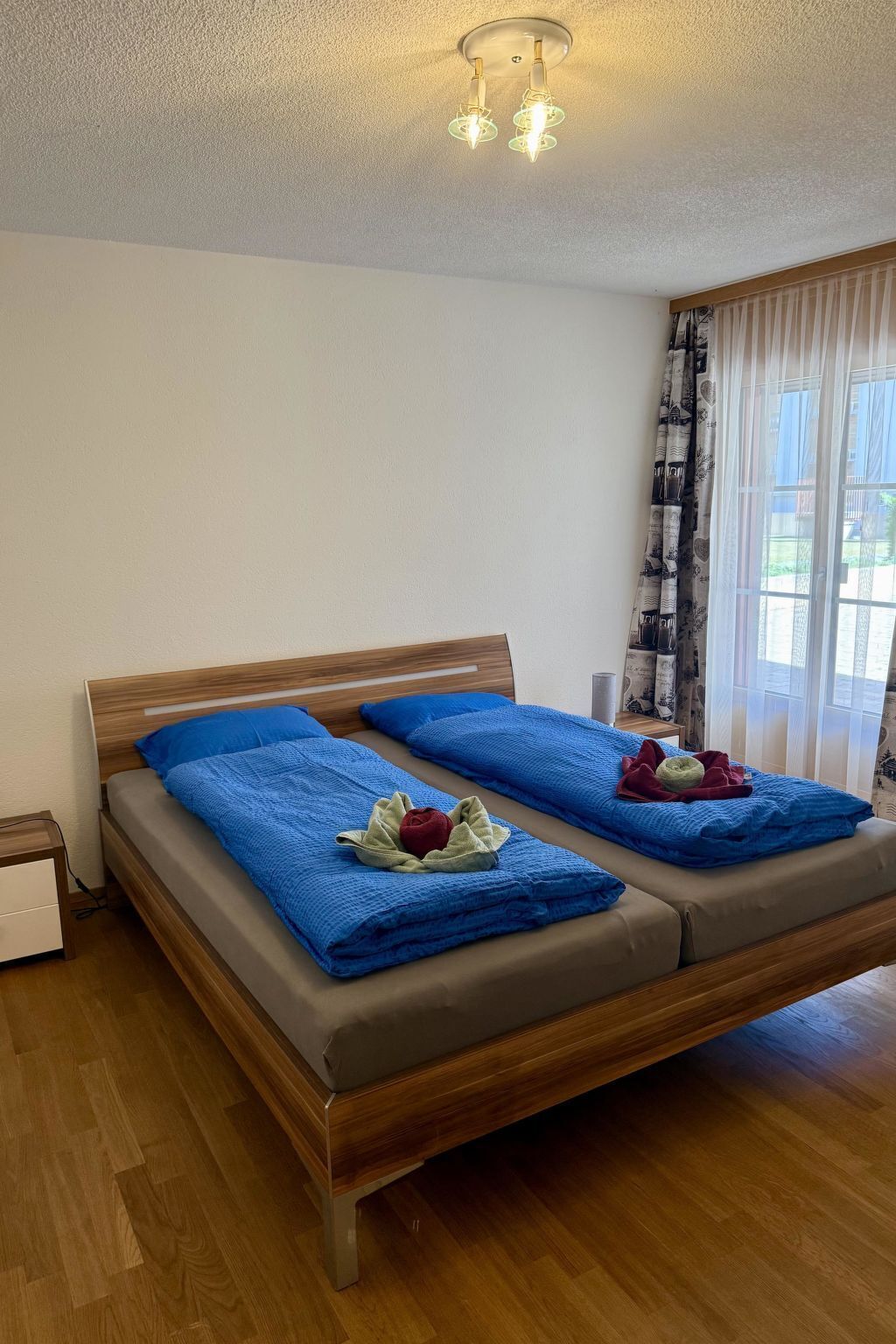 A double bed with a wooden frame, two pillows, and a blue blanket.