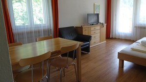 Ett rum med ett matbord och stolar i trä, en svart lädersoffa, ett träskåp och en säng med vita sängkläder.