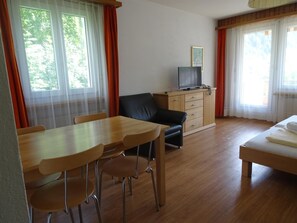 A room with a wooden dining table, chairs, a black leather sofa, a wooden cabinet, and a bed with white bedding. - Leuca 31 # 2-bed apartment, Dusche, WC 2-Bettwohnung, Dusche, WC by Interhome (Leukerbad)