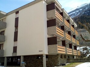 A multi-story hotel with balconies, a stone facade, and a view of snow-capped mountains. - Leuca 31 # 2-bed apartment, Dusche, WC 2-Bettwohnung, Dusche, WC by Interhome (Leukerbad)