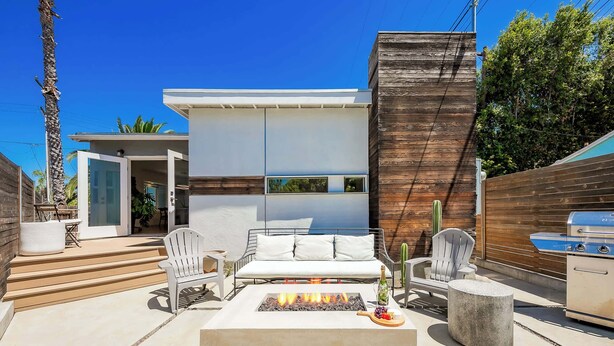 Een modern terras buiten met vuurkorf, zitplaatsen en een barbecue.