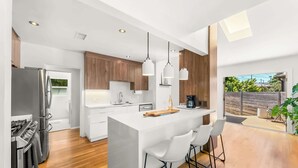 Een moderne keuken met een centraal kookeiland, witte barkrukken en hanglampen.
