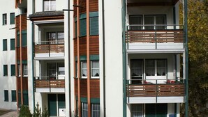 Um edifício residencial de vários andares, com varandas, área de pátio com mobiliário de exterior e um pequeno jardim.