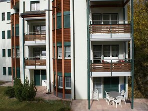 Ein mehrstöckiges Wohngebäude mit Balkonen, einer Terrasse mit Gartenmöbeln und einem kleinen Garten.