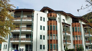 Um edifício de vários andares com varandas, telhado plano e área gramada na frente.