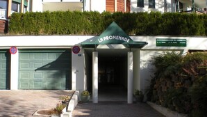 Entrada de um edifício com toldo verde identificada como 'LA PROMENADE' e um aviso indicando 'FELIENWOHUNGEN ZU VERMIETEN'.