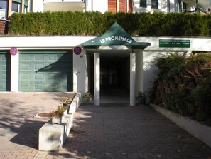 Ein Gebäudeeingang mit einer grünen Markise, auf der 'LA PROMENADE' steht, und einem Schild mit der Aufschrift 'FERIENWOHNUNGEN ZU VERMIETEN'.