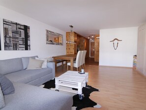 Ein Wohnzimmer mit grauem Sofa, einem Holzesstisch und einem weißen Couchtisch.
