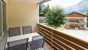 Un balcone con tavolo e sedie, affaccia su un paesaggio montano e un edificio con la scritta 'Confit'.