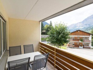 Ein Balkon mit Tisch und Stühlen, der auf eine Berglandschaft und ein Gebäude mit der Aufschrift 'Confit' blickt.