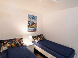 Ein Schlafzimmer mit zwei Einzelbetten, einem Nachttisch mit Lampe und einem Poster an der Wand.