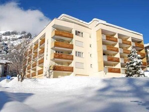 Ein mehrstöckiges Hotel mit Balkonen, einem Parkplatzschild und verschneiter Landschaft.