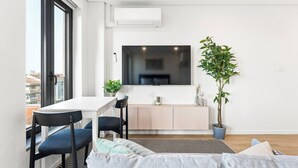 Un salon moderne comprenant un coin repas, une grande fenêtre, un téléviseur à écran plat, une plante en pot et un tapis à rayures.