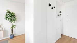 Une chambre moderne et minimaliste, avec une plante en pot, une armoire blanche et une porte surmontée d’une petite étagère.