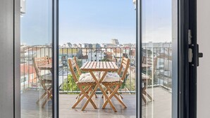 Un balcon avec une table et des chaises en bois, une porte vitrée et une vue sur la ville.