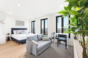 A modern hotel room with a bed, a sofa, a desk, and a large window. - Modern Studio | Steps from Casa da Música (Porto)