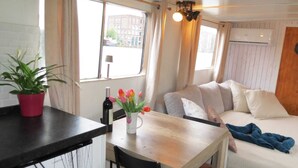 A room with a dining table, chairs, a potted plant, a bottle of wine, and a vase with flowers. - Aloha: An authentic houseboat just 14 minutes from Amsterdam and close to Zaanse Schans (Wormer)