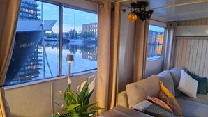 A room with a large window, a sofa, a table, and a potted plant. - Aloha: An authentic houseboat just 14 minutes from Amsterdam and close to Zaanse Schans (Wormer)