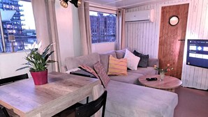 A cozy room with a wooden dining table, a sofa with cushions, a small round table, and a potted plant. - Aloha: An authentic houseboat just 14 minutes from Amsterdam and close to Zaanse Schans (Wormer)