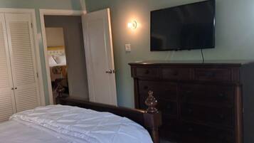 A bedroom with a bed, a ceiling fan, a TV, a dresser, and a door leading to another room.