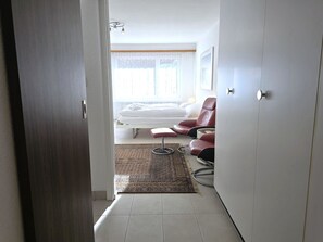 Ein Hotelzimmer mit einem Bett, zwei roten Sesseln, einem kleinen Teppich und einer Tür zu einem anderen Raum.