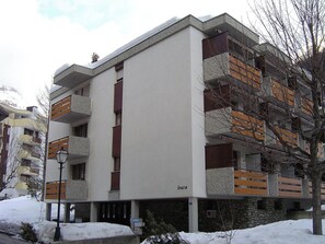 Ein mehrstöckiges Gebäude mit Balkonen, einem Schild mit der Aufschrift 'leuca' und Schnee auf dem Boden.