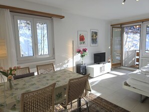 Ein gut beleuchteter Raum mit Esstisch, Stühlen, Fernseher und einer Couch.