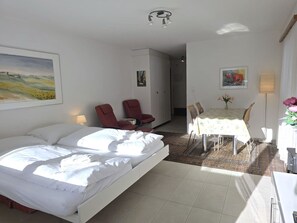 Habitación de hotel con cama, una mesa de comedor con sillas, una silla roja y un cuadro en la pared.