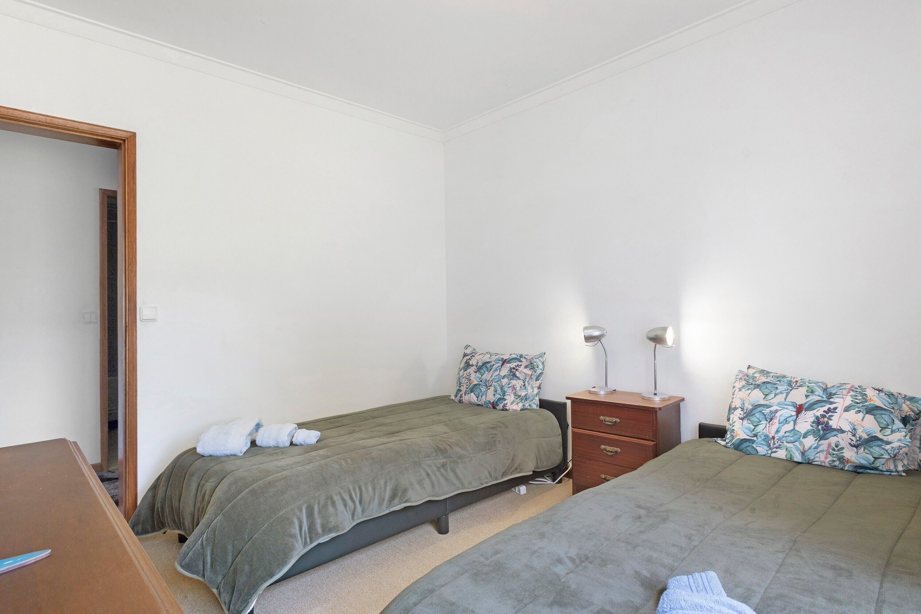 A bedroom with two beds, a wooden dresser, and a nightstand with a lamp.