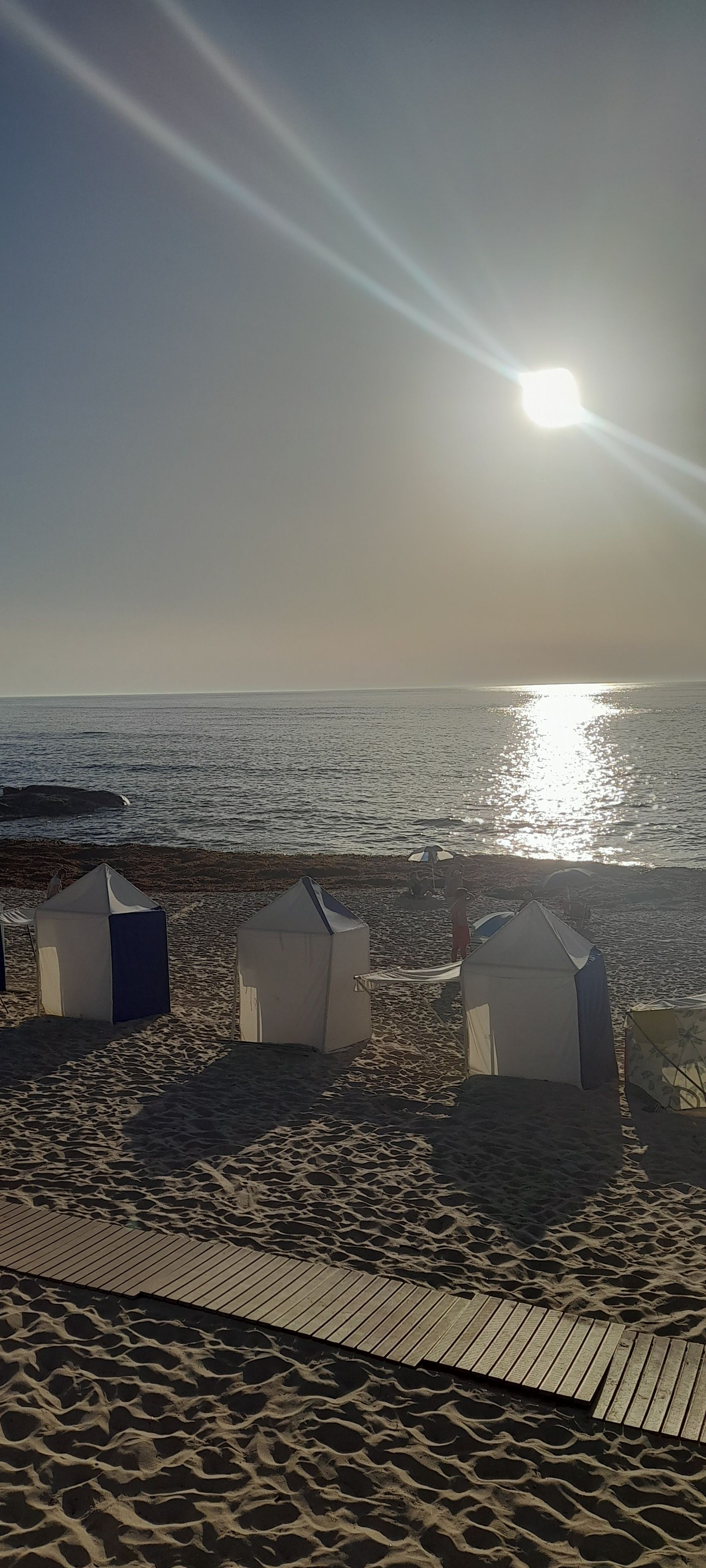 A beach with several tents and a wooden walkway.